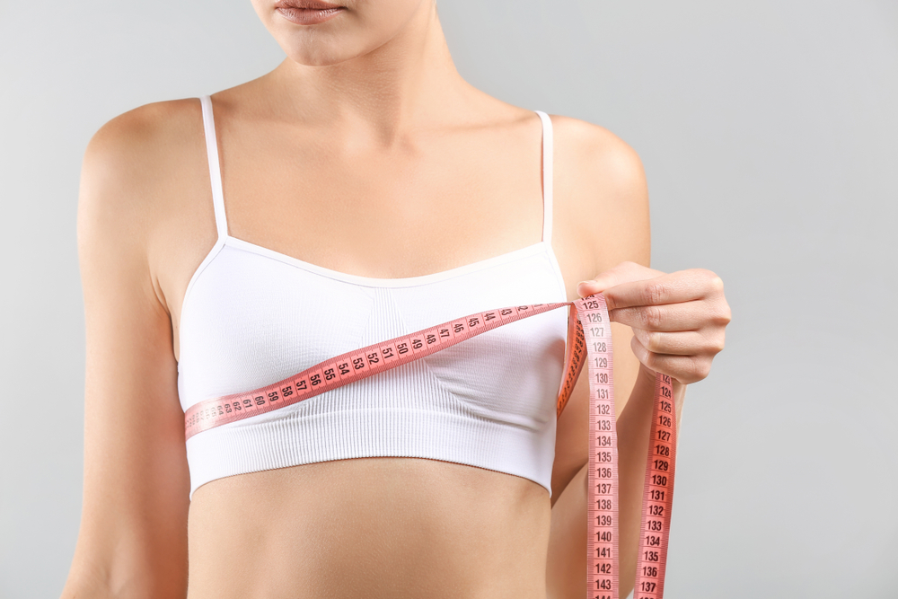 Close up of a woman measuring her breasts, in need of more information about breast lifts.