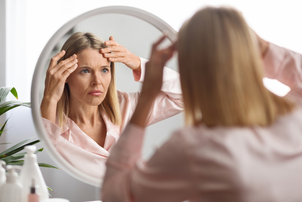 Woman looking at her forehead wrinkles in the mirror, in need of brow lift or Botox treatment.