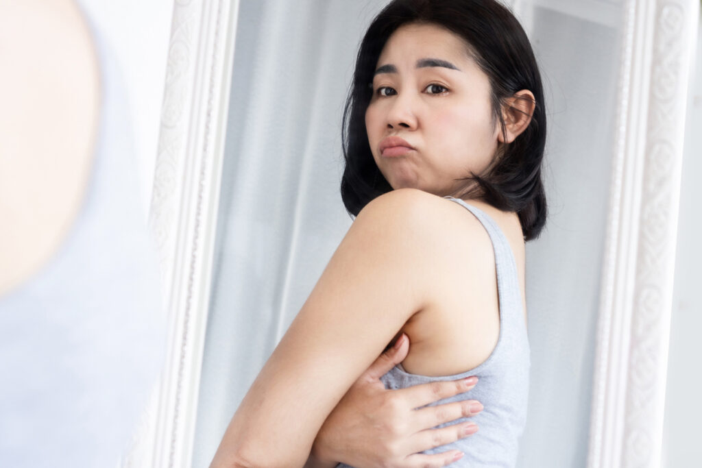 Young asian woman looking at her back in the mirror, perhaps wanting a bra line back lift. Young asian woman looking at her back in the mirror, perhaps wanting a bra line back lift.