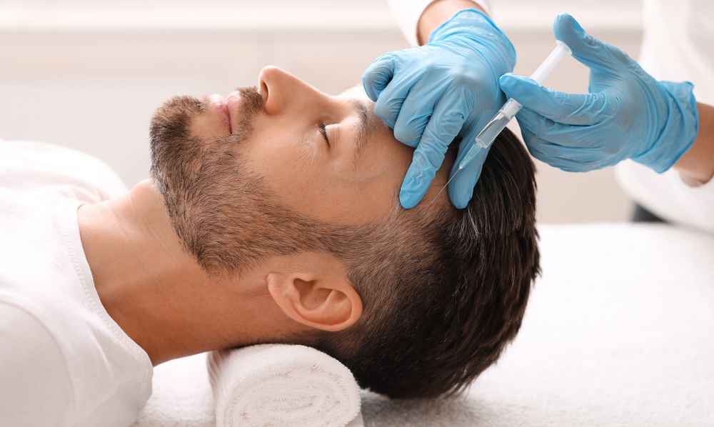 Side profile of a man laying down and receiving PRP hair restoration injections to his scalp in a spa-like setting. Side profile of a man laying down and receiving PRP hair restoration injections to his scalp in a spa-like setting.