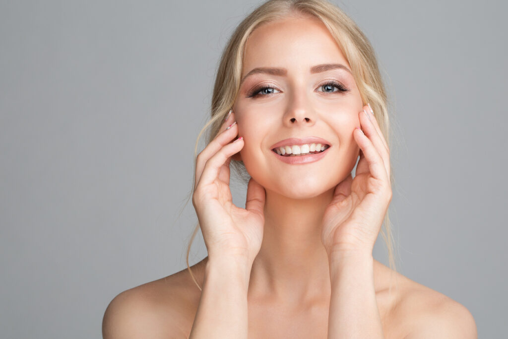 Smiling woman touching her cheek looking fully healed after her facelift recovery. Smiling woman touching her cheek looking fully healed after her facelift recovery.
