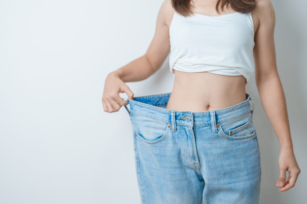 Woman holding oversized jeans after weight loss, while considering body lift surgery. Woman holding oversized jeans after weight loss, while considering body lift surgery.