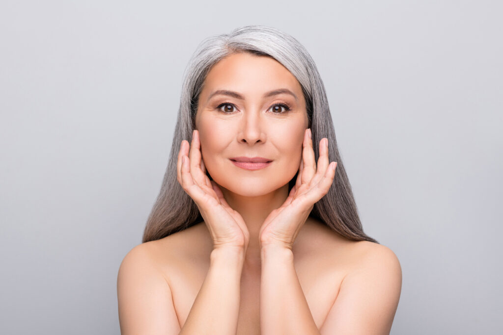 Woman touching her cheek while considering fillers or facial fat grafting for volume loss. Woman touching her cheek while considering fillers or facial fat grafting for volume loss.