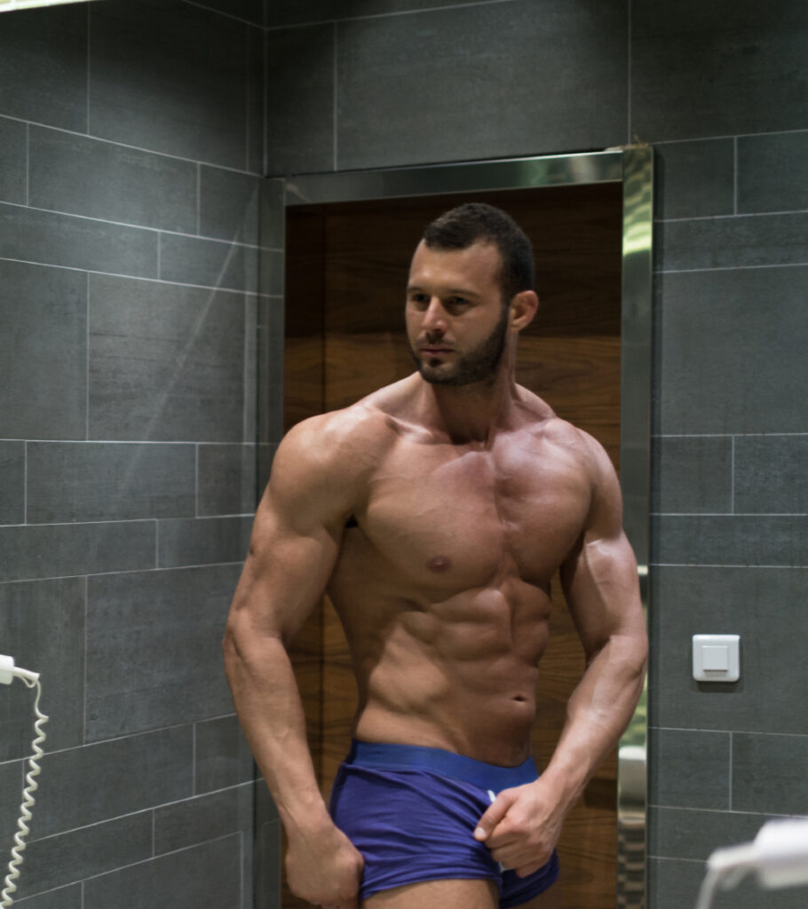 Shirtless man examining his abdomen in a mirror Shirtless man examining his abdomen in a mirror